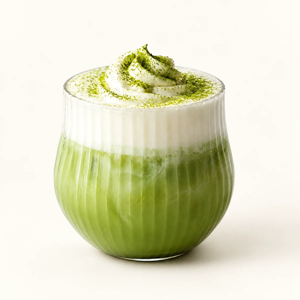 Hot matcha latte in a ribbed glass topped with whipped cream and a dusting of matcha