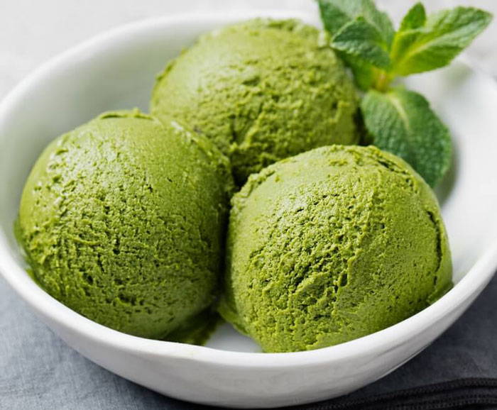 Green matcha ice cream scoops in a white bowl with mint leaves