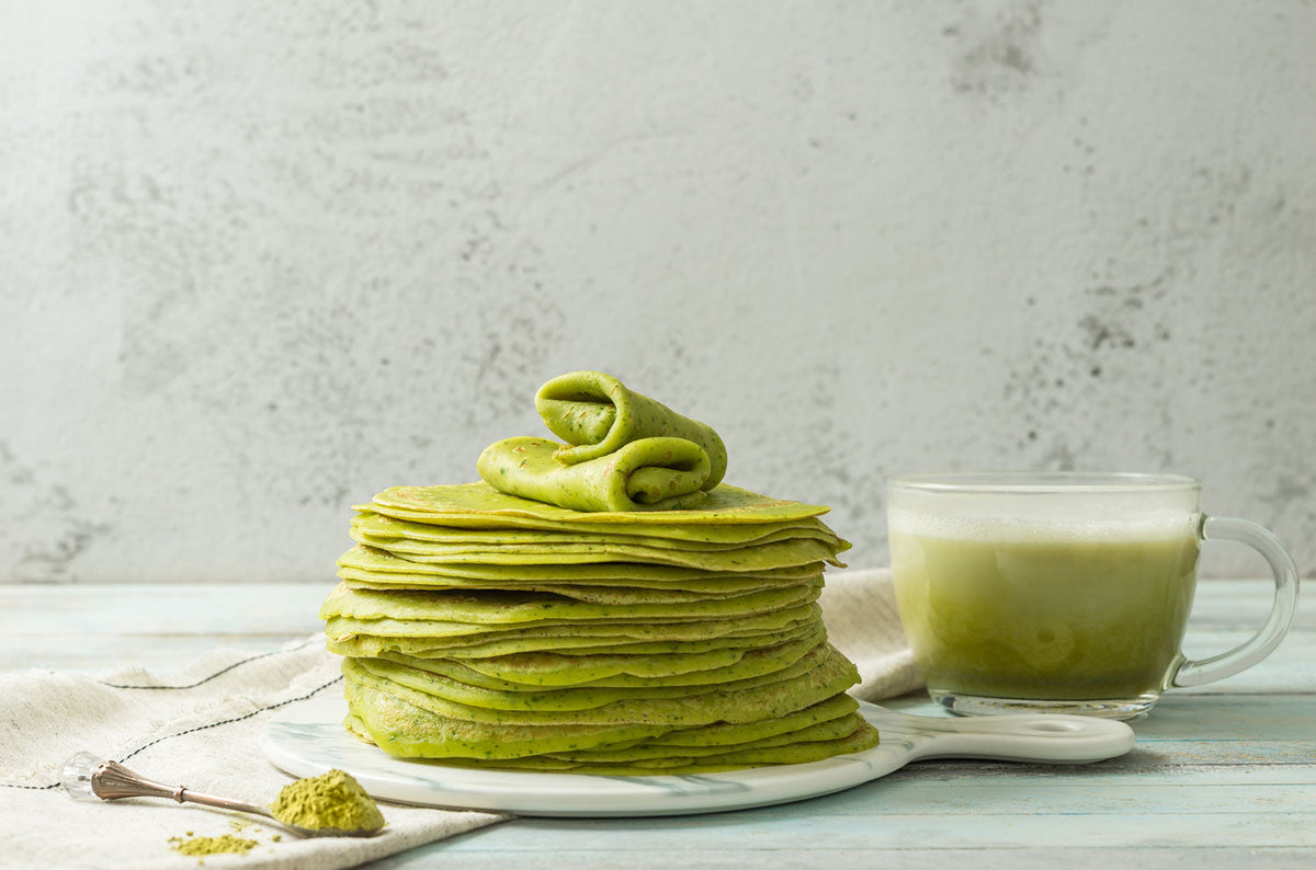 bowl of matcha tea bet to bowl of green tea powder with whisk and bamboo scoop
